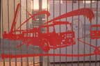 cutout of red fire engine superimposed on fence grating